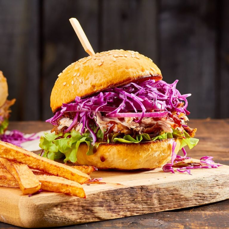 Two sandwiches with pulled pork, french fries and glass of beer on old wooden background. Rustic style